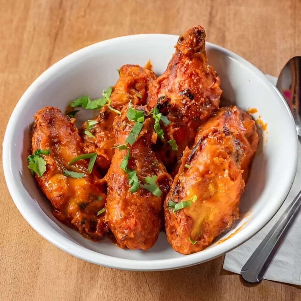 A white bowl filled with Pataka Indian Fusion Cuisine's vibrant orange chicken wings, garnished with fresh cilantro.