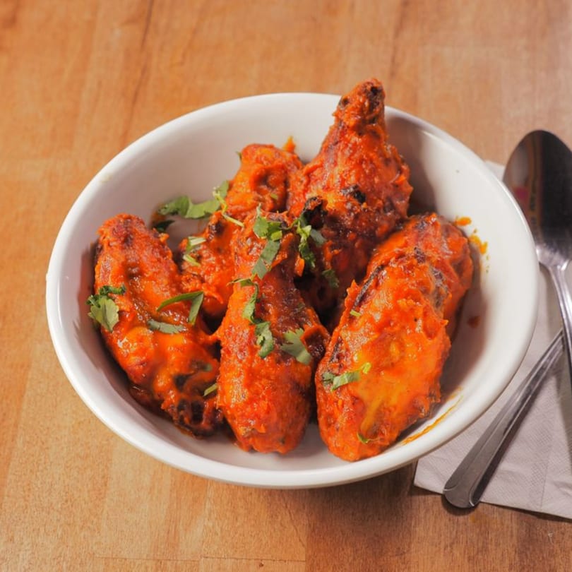 A white bowl filled with vibrant orange Pataka Indian Fusion chicken wings, garnished with fresh cilantro.