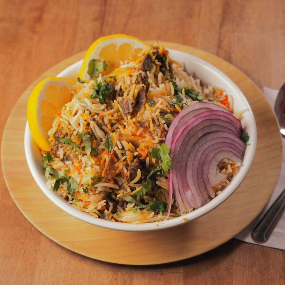 Pataka Indian Fusion Cuisine's biryani, garnished with lemon wedges, red onion, and fresh cilantro.