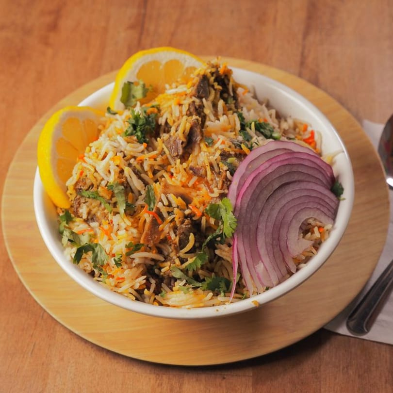 Pataka Indian Fusion Cuisine's biryani, garnished with lemon wedges, red onion, and fresh cilantro.