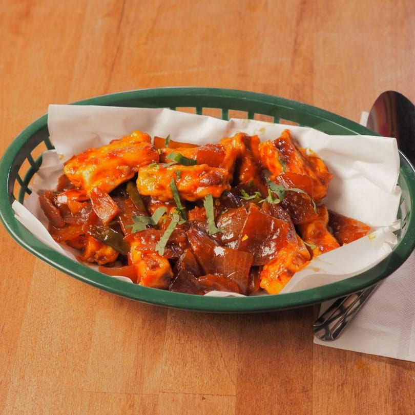 Pataka Indian Fusion Cuisine's chili paneer, a vibrant orange dish with onions and cilantro in a green basket.