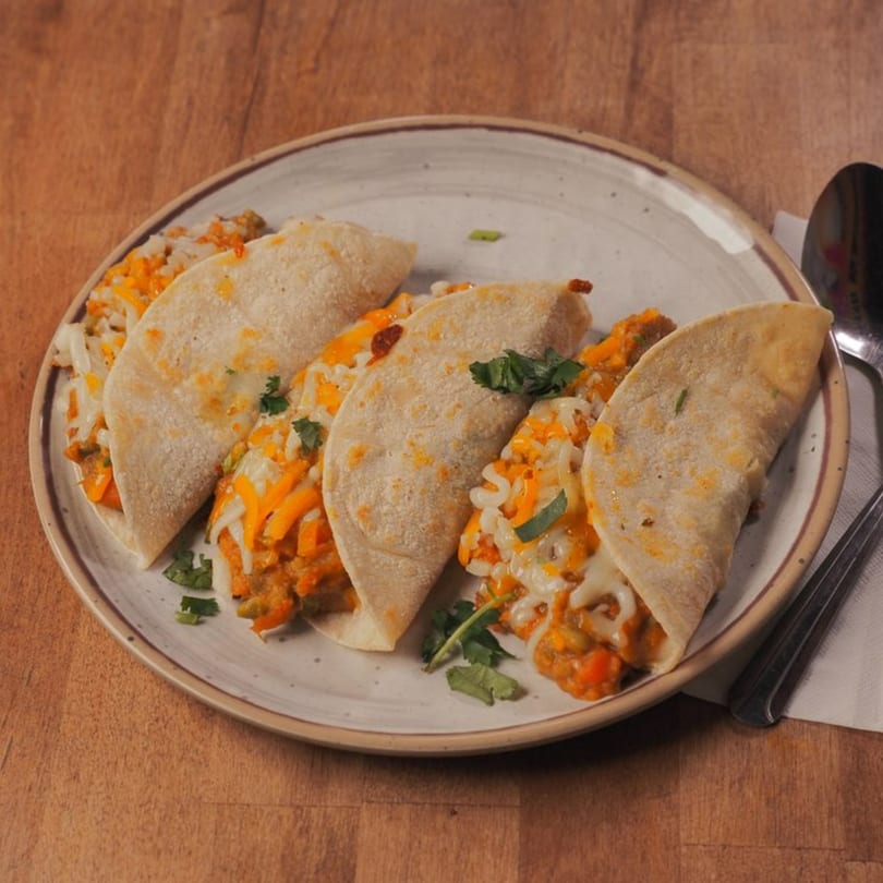 Four Indian fusion tacos with melted cheese and cilantro on a white plate.