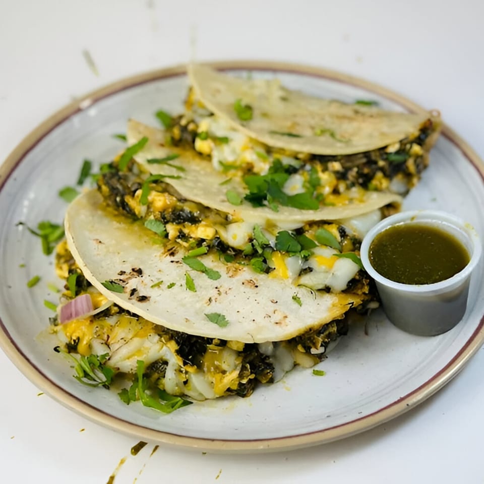 Three Pataka Indian Fusion Cuisine tacos with green sauce on a white plate.