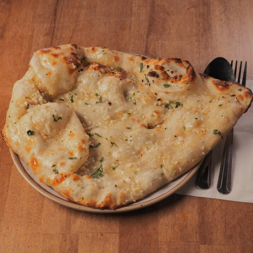 Pataka Indian Fusion Cuisine's garlic naan, golden brown and garnished with fresh herbs, on a plate.