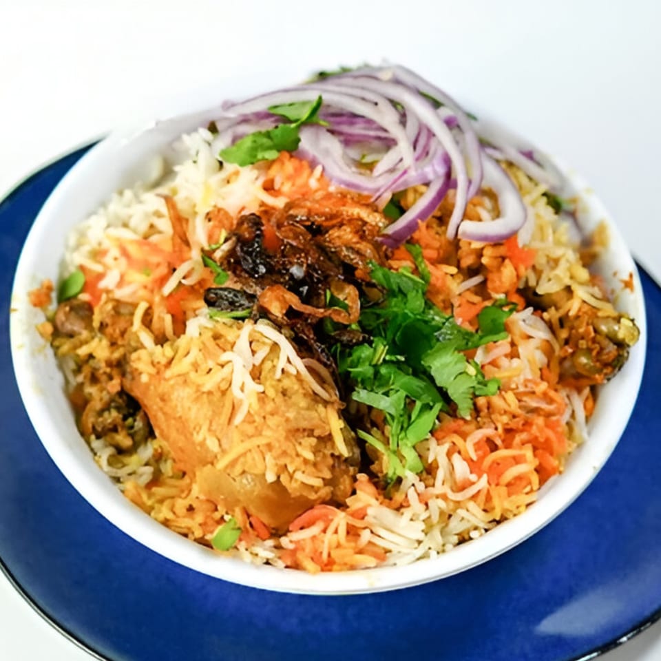 Pataka Indian Fusion Cuisine's chicken biryani, garnished with red onions, cilantro, and fried onions.